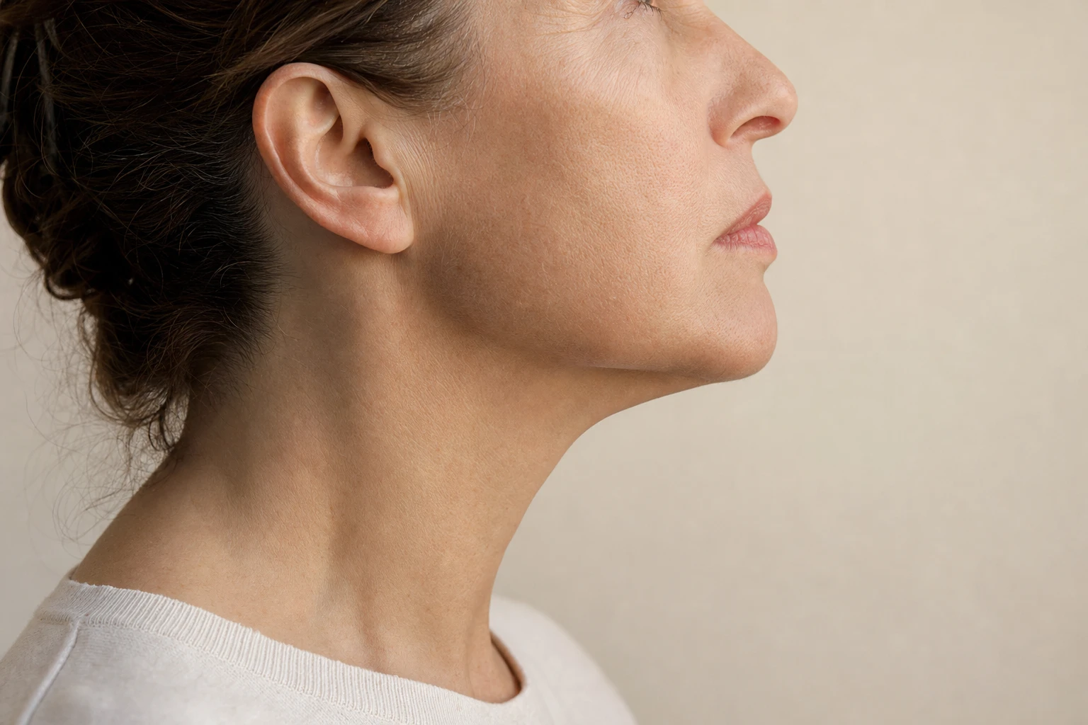 Bas du visage d'une femme fictive vu de profil, mâchoire détendue, la lumière rasante dessinant l'angle de la mâchoire, sur un fond clair et sobre.