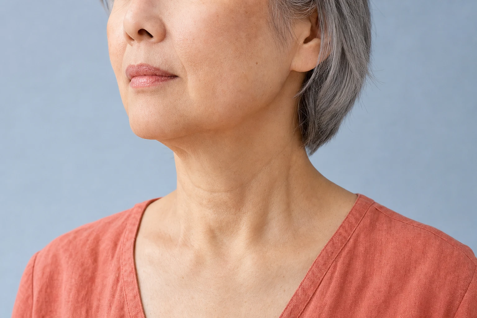 Lower face and neck of a grey-haired woman at rest in three-quarter view, with slight natural folds beneath the chin.
