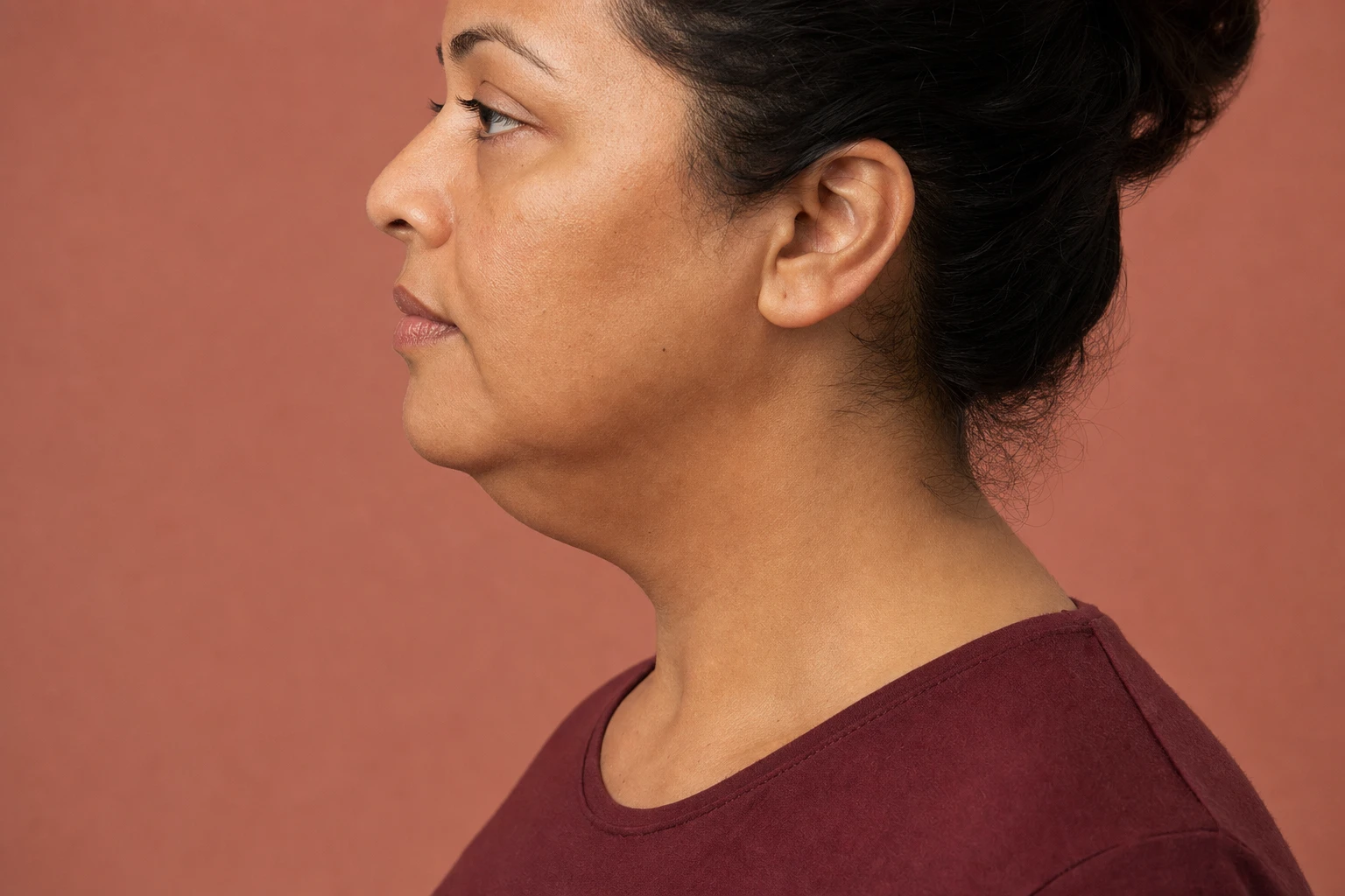 Woman in a relaxed side profile, with the underside of her chin and neck visible against a clay-coloured background.