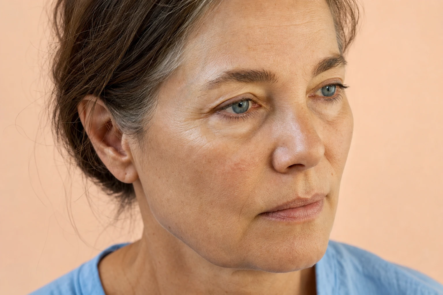 Three-quarter view of a fictional woman's face, with a slight hollow under the eye, lit with soft light.